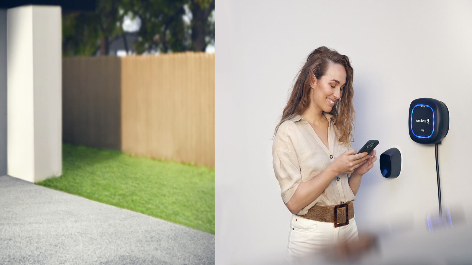Das Bild zeigt eine Frau, die lächelnd ihr Smartphone bedient und neben einer an der Wand montierten Wallbox-Ladestation steht.