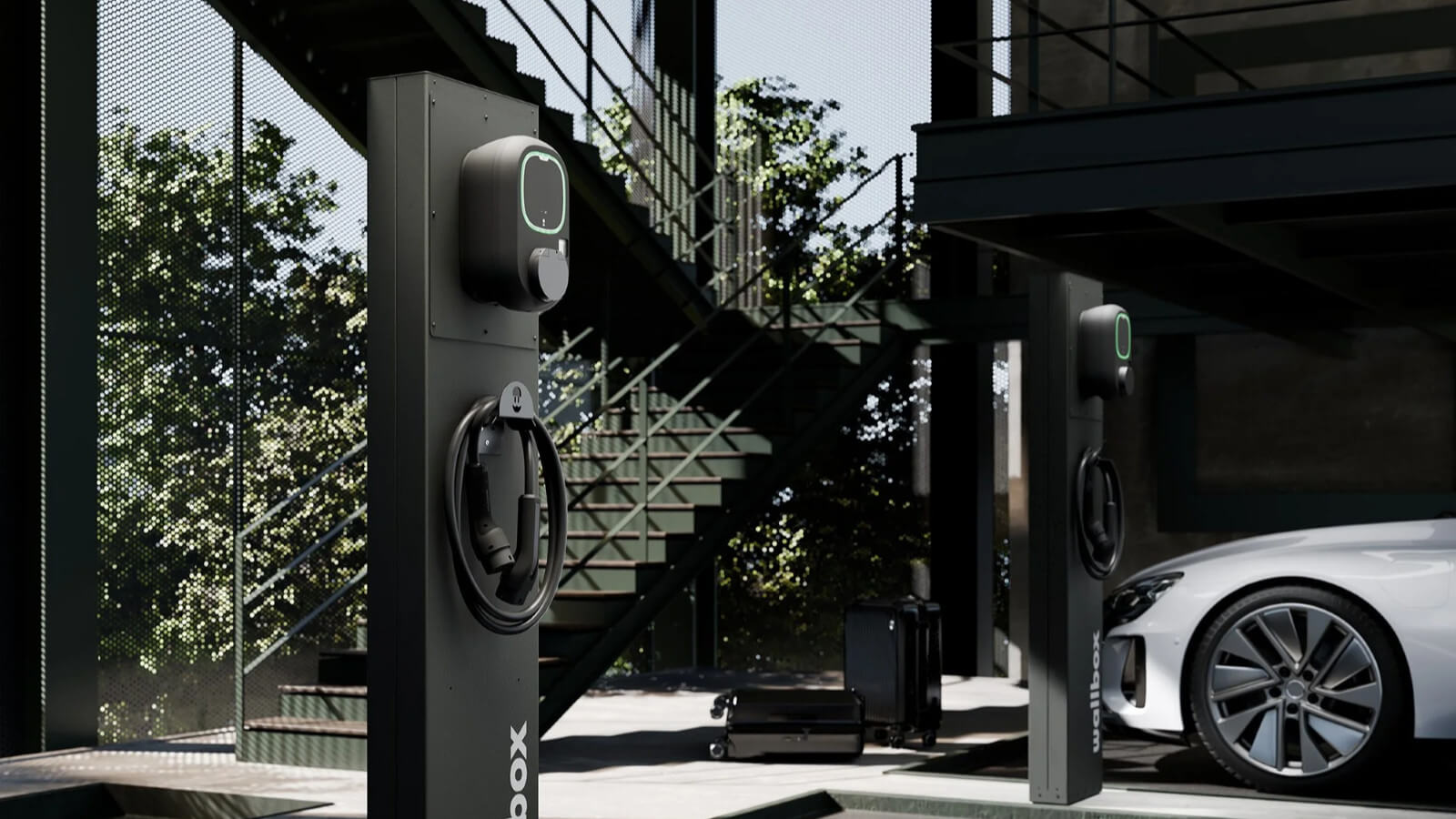 Das Bild zeigt zwei schwarze Ladesäulen mit Wallboxen und Ladekabeln. Eine weiße Limousine ist an einer der Säulen geparkt. Im Hintergrund ist eine dunkle Metalltreppe zu sehen.