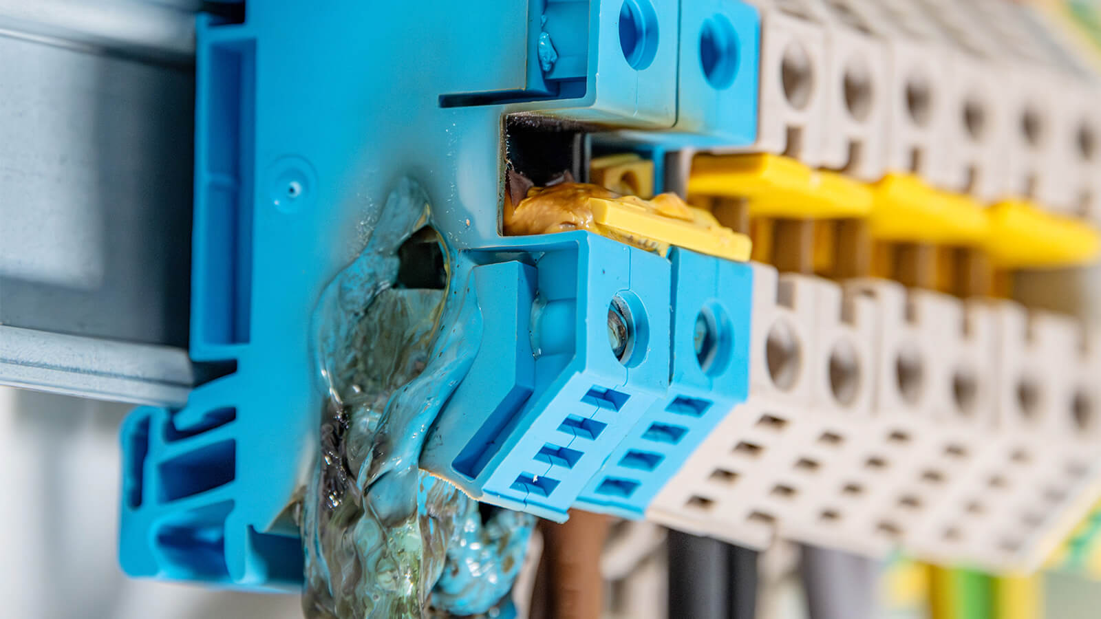 Das Bild zeigt mehrere blaue und gelbe Kunststoffklemmen, von denen eine stark angeschmolzen und mit geschmolzenem Material bedeckt ist.