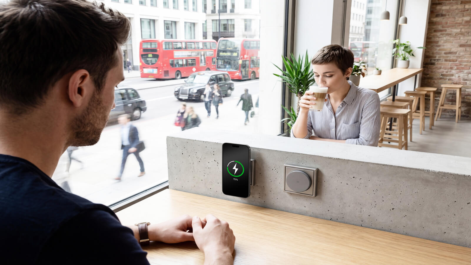 Das Bild zeigt ein Café mit Menschen am Tisch und einer magnetischen Ladestation für ein Smartphone in der Wand.