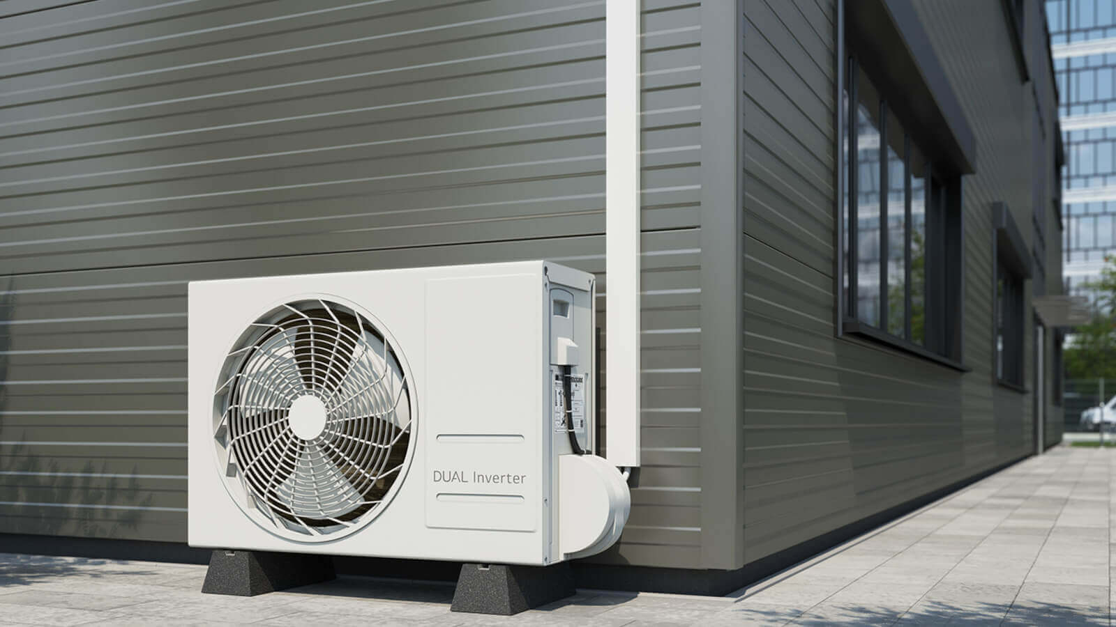Das Bild zeigt eine außen am Gebäude installierte weiße Wärmepumpen- oder Klimaanlagen-Außeneinheit (Dual Inverter) auf zwei Sockeln. Die Zuleitung verläuft in einem weißen, senkrechten Kabelkanal an der Fassade und führt geschützt in das Gerät.