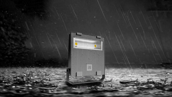 Das Bild zeigt einen rechteckigen Strahler im Regen. Der Boden ist nass, und Regentropfen fallen sichtbar herab