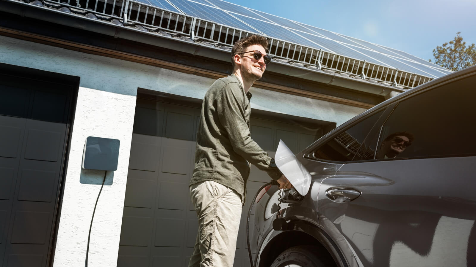 Ein Mann steht neben seinem Auto und lädt es mit Solarenergie auf.