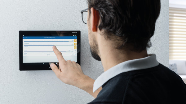 LUXORliving CP10: Innenstation für smarte Türkommunikation und zentrale Smart Home-Steuerung Das Bild zeigt eine Person, die das schwarze LUXORplay-Display bedient. Die Person tippt auf den Touchscreen, auf dem eine detaillierte Ansicht mit verschiedenen Einstellungsoptionen zu sehen ist. Das Menü ermöglicht die Steuerung von Funktionen wie Beleuchtung und Automatik. Der Benutzer scheint eine spezifische Einstellung zu justieren.