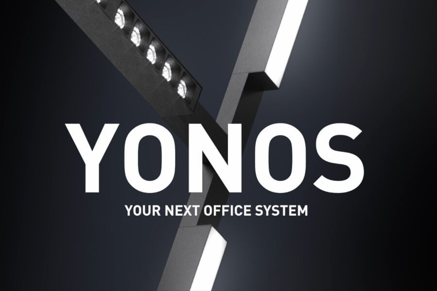 TRILUX YONOS Das Bild zeigt den Ausschnitt eines Y-förmigen Leuchtensystems vor dunklem Hintergrund. Im Vordergrund steht der Schriftzug „YONOS“ in Weiß, darunter die Beschreibung „YOUR NEXT OFFICE SYSTEM“.
