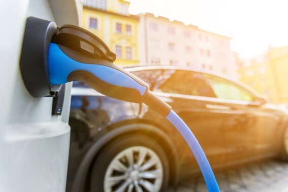 Das Bild zeigt eine E-Ladesäule. Im Hintergrund steht ein schwarzes Fahrzeug.