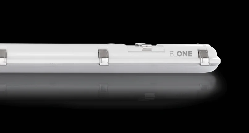 Das Bild zeigt eine weiße, längliche LED-Leuchte mit Metallklammern zur Befestigung. Auf der rechten Seite ist der Schriftzug „BL ONE“ zu sehen. Die Leuchte liegt auf einem spiegelnden Untergrund vor schwarzem Hintergrund.
