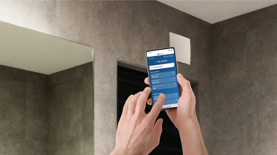 Zwei Hände halten ein Smartphone in Richtung einer oben an einer Wand befestigten Lüftung. Auf dem Display des Smartphones ist die MAICO@NFC-App erkennbar. 