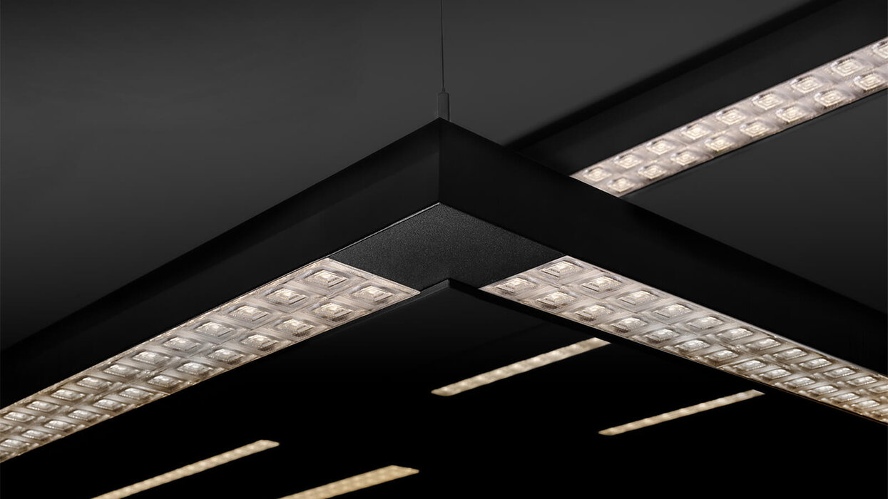 Das Bild zeigt eine Detailaufnahme schwarzer, rechtwinklig angeordneter LED-Lichtbänder mit prismatischen Optiken vor dunklem Hintergrund.