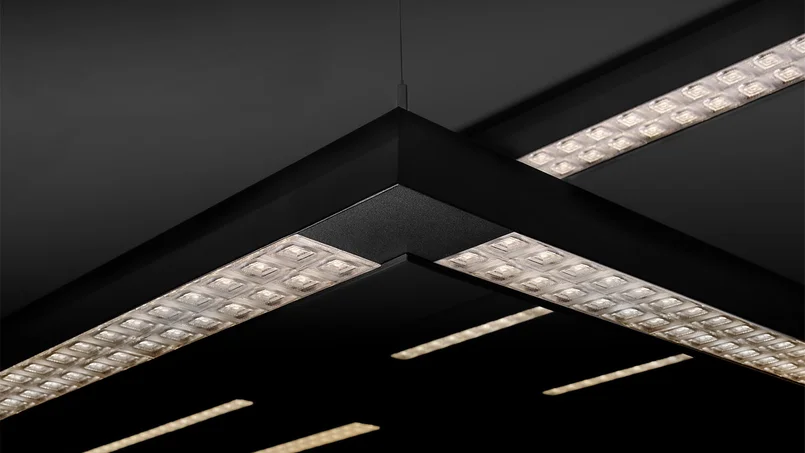 Das Bild zeigt eine Detailaufnahme schwarzer, rechtwinklig angeordneter LED-Lichtbänder mit prismatischen Optiken vor dunklem Hintergrund.