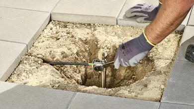 Montage eines Erdungssystems im Außenbereich: Eine Person installiert einen Erdungsstab im Boden zwischen Pflastersteinen.