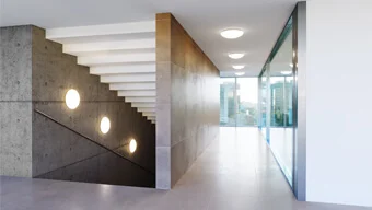 Moderner Flur mit Deckenleuchten. Im Hintergrund großes Fenster mit Blick nach draußen.