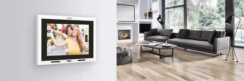 Das Bild zeigt ein modernes Wohnzimmer mit einem an der Wand montierten Touchdisplay zur Türkommunikation, auf dem zwei Besucher angezeigt werden.