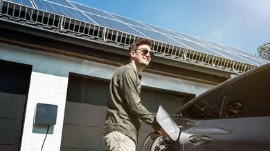 Ein Mann steht neben seinem Auto und lädt es mit Solarenergie auf.