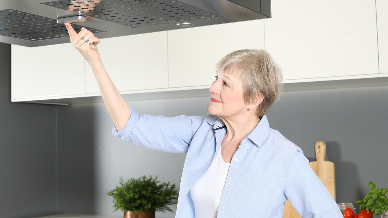 Das Bild zeigt eine ältere Person in einer modernen Küche, die eine Dunstabzugshaube bedient.