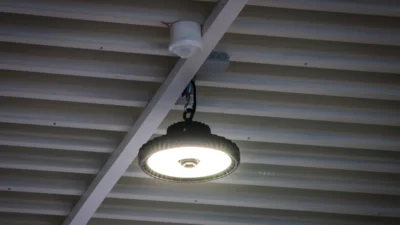 Das Bild zeigt eine Decke mit Holzstreben, an der ein runder Hallenstrahler aus der Serie LIGHTSHOWERsmart hängt