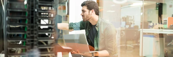 Das Bild zeigt eine Person mit Laptop vor einem Server.