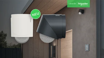 Ein schwarzer Bewegungsmelder, der an der Hauswand montiert ist und eine ebenfalls montierte Leuchte.