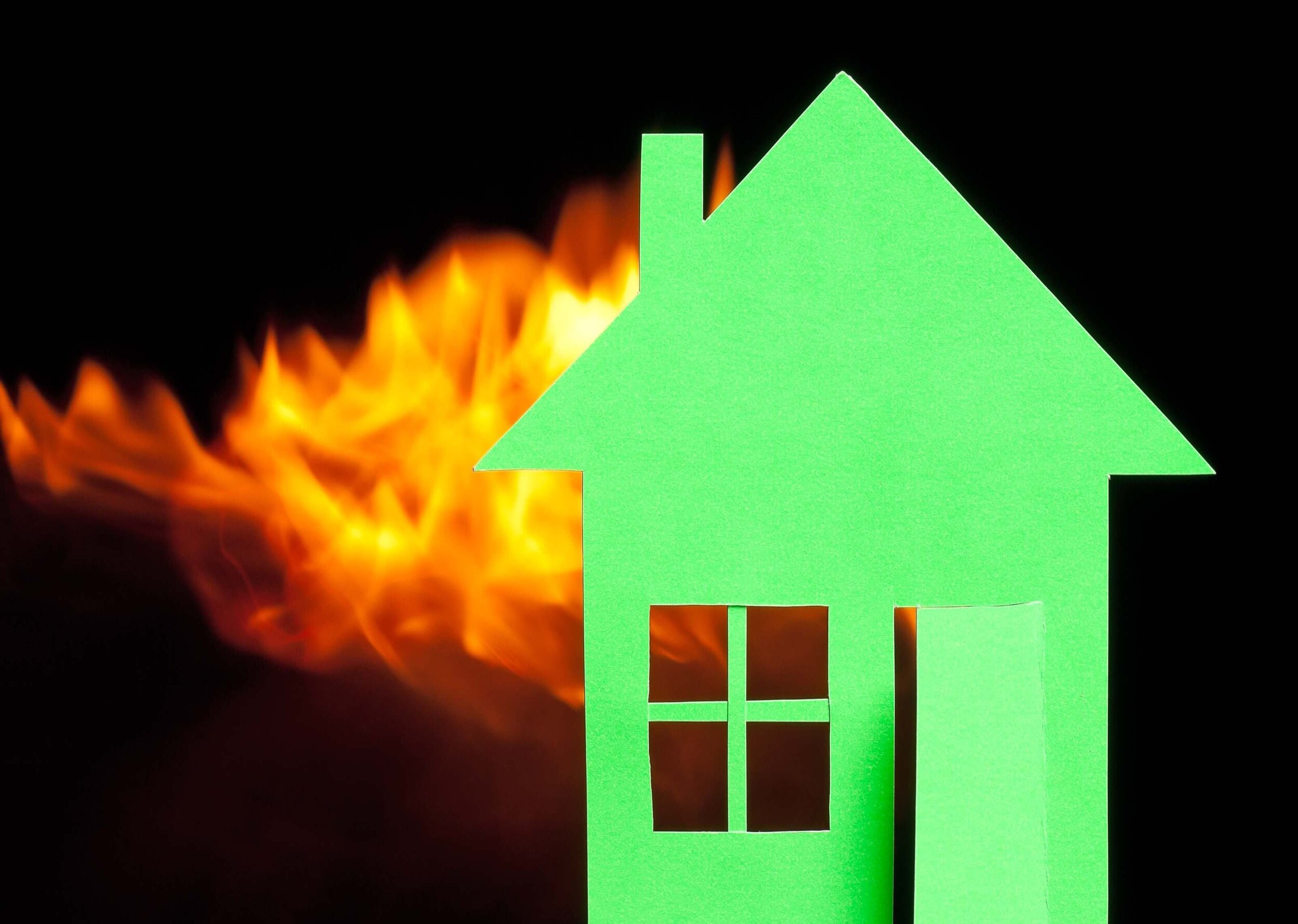 Das Bild zeigt symbolhaft ein grünes Haus, in dem Feuer ausgebrauchen ist. Das Haus steht vor einem schwarzen Hintergrund.