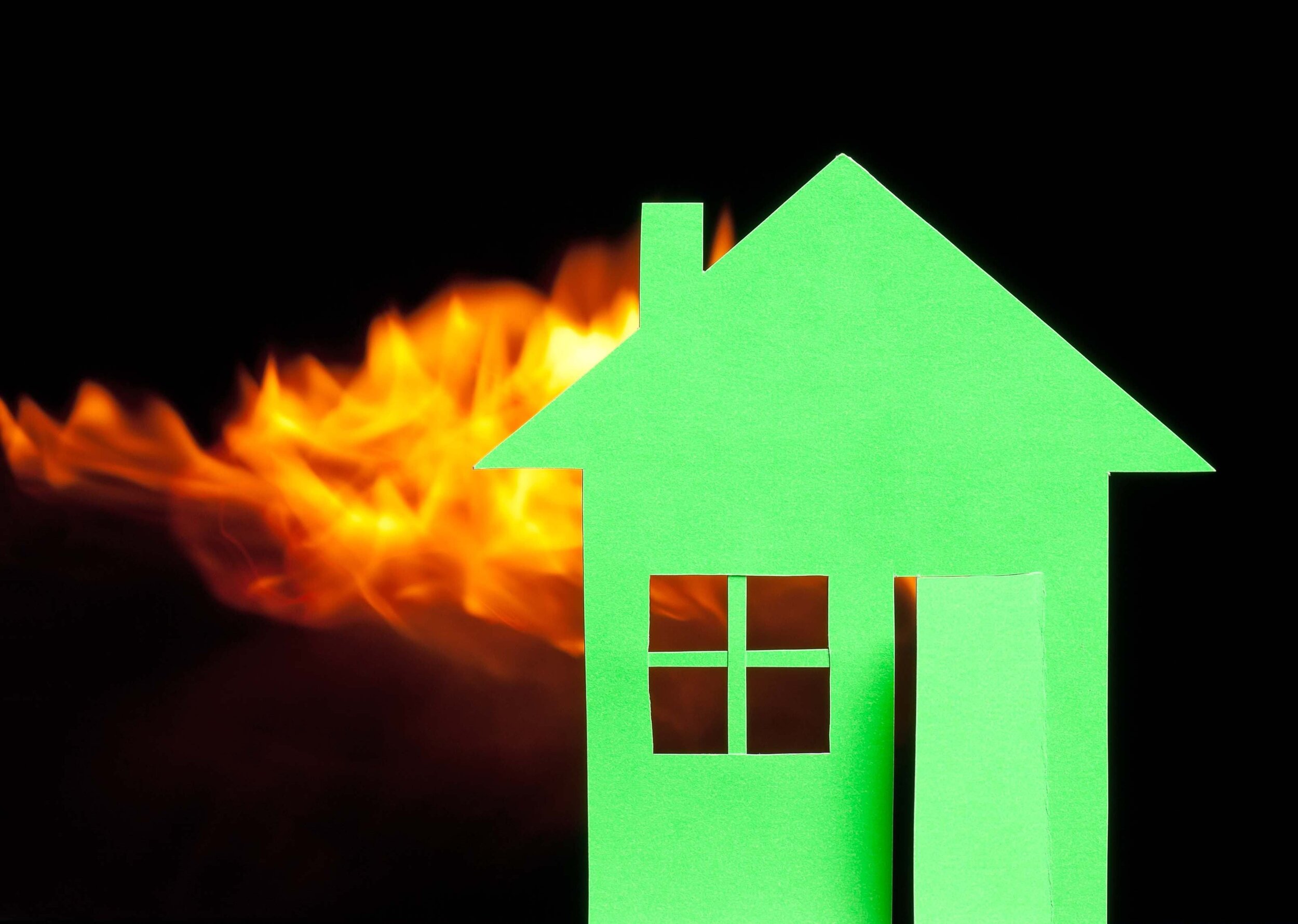 Das Bild zeigt symbolhaft ein grünes Haus, in dem Feuer ausgebrauchen ist. Das Haus steht vor einem schwarzen Hintergrund.