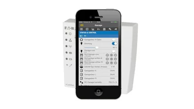 Das Bild zeigt einen weißen xComfort Smart Home Controller schräg hinter einem schwarzen Smartphone. Auf dem Display des Smartphone ist die App-Funktionen zum Steuerung des Systems abgebildet.