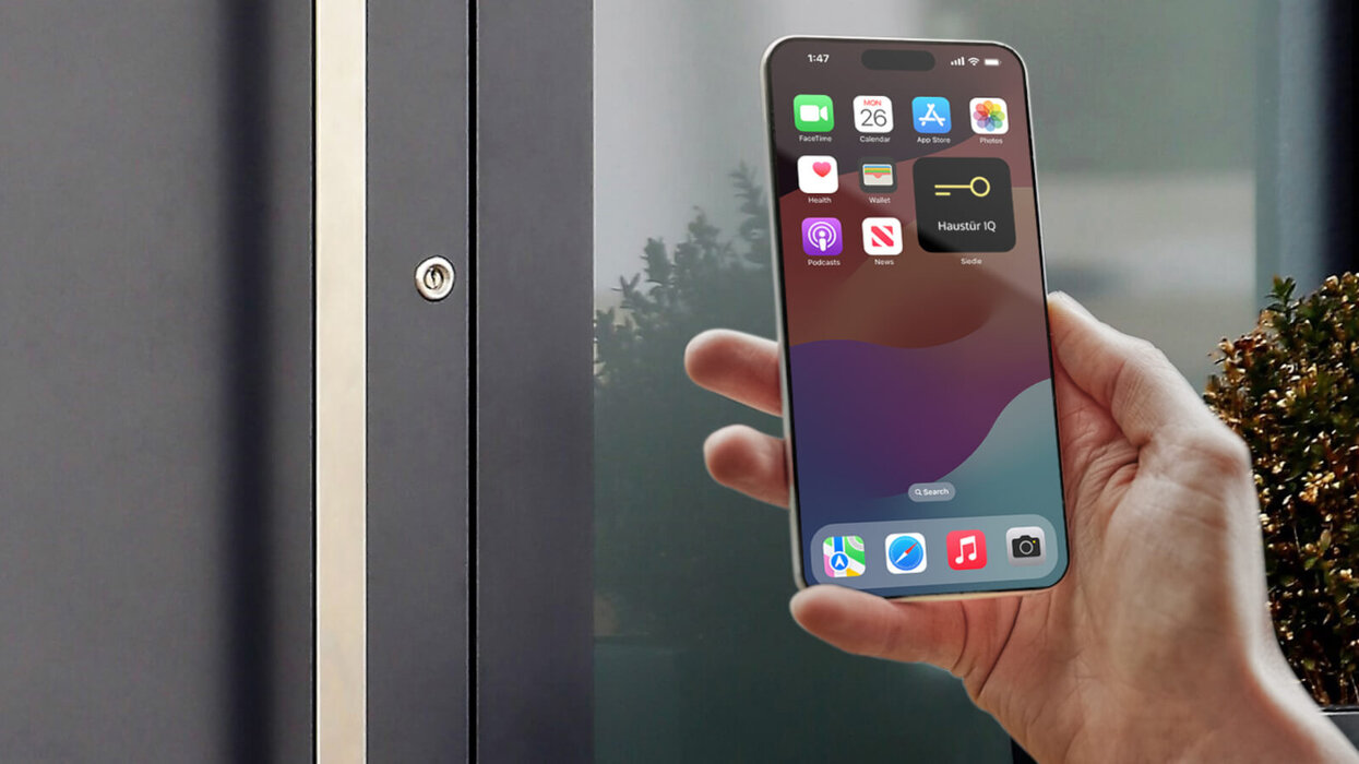 Eine Person hält ein Smartphone mit geöffneter App in der Hand, daneben ist ein Türschloss an einer Haustür zu sehen.