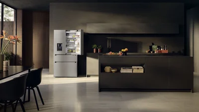 Das Bild zeigt eine moderne, stilvolle Küche mit offenem Kühlschrank, Kochinsel und eleganter Einrichtung in dunklen Farbtönen.