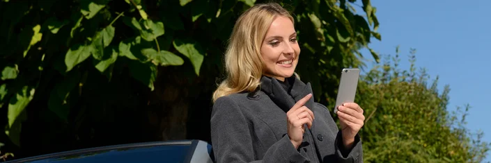 Das Bild zeigt eine Frau im Freien, die lächelnd ihr Smartphone benutzt.