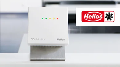 Das Bild zeigt in Großaufnahme einen weißen CO2-Monitor, der auf einem Tisch steht. In der rechten oberen Bild-Ecke ist das Logo des Herstellers Helios abgebildet.