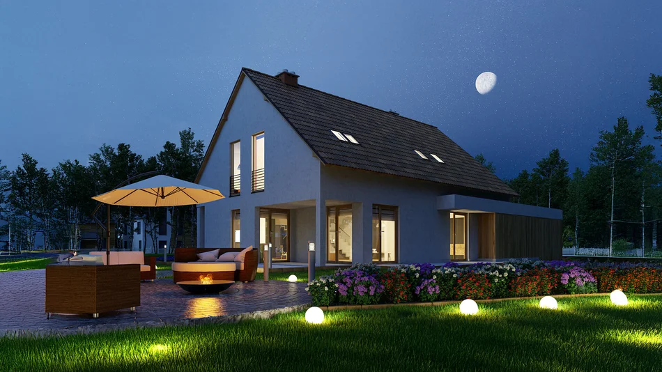 Das Bild zeigt ein modernes Einfamilienhaus bei Nacht. Das Haus hat ein Satteldach, große Fenster und ist von einem beleuchteten Garten mit Blumen, Rasen und einer Terrasse mit Sitzmöbeln umgeben. Der Himmel ist dunkel mit sichtbarem Mond und Sternen.