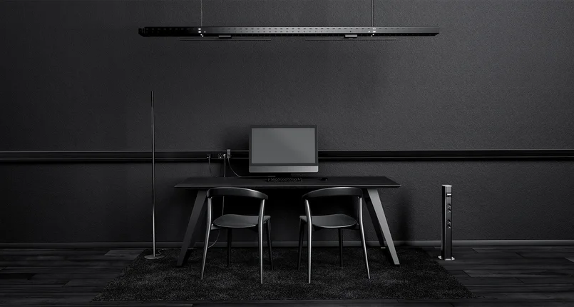 An einer Wand steht ein rechteckiger Tisch, auf dem sich ein Bildschirm und eine Tastatur befinden. Vor dem Tisch stehen 2 Stühle. Auf der einen Seite des Schreibtisches steht eine schlanke Stehleuchte. Über dem Tisch hängt eine moderne Hängeleuchte. Die Kabel der Elektrogeräte laufen zu einer Leiste, die parallel zum Boden an der Wand verläuft. Alle Gegenstände ebenso wie die Wand und der Boden sind schwarz.