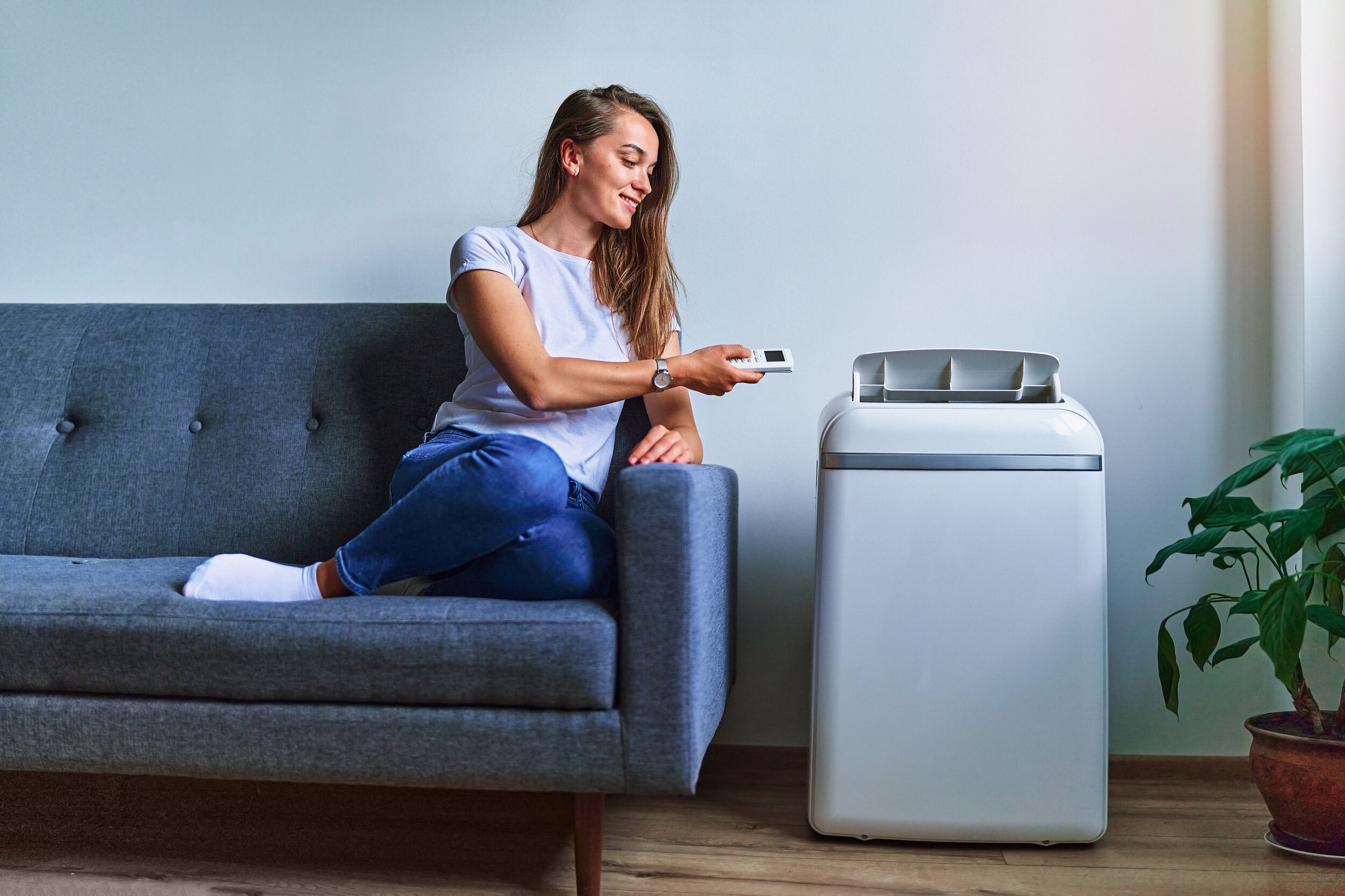 Dieses Bild zeigt eine Frau, die auf dem Sofa sitzt und auf ihre Mobile Klimaanalage schaut, die rechts neben ihr steht.