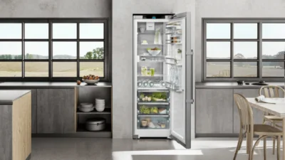 Freistehender Kühlschrank von Liebherr in der Farbe Weiß und der geöffnet ist und in eine elegante schwarzbraune Küchenzeile integriert wurde.