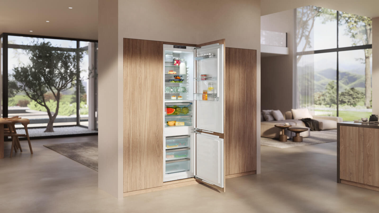 Das Bild zeigt eine moderne, offene Küche mit einem integrierten Einbau-Kühl-Gefriergerät. Die Türen des Kühlschranks sind geöffnet und geben den Blick auf übersichtlich eingeräumte Lebensmittel frei. Große Fenster und viel Tageslicht verleihen dem Raum eine helle, elegante Atmosphäre.