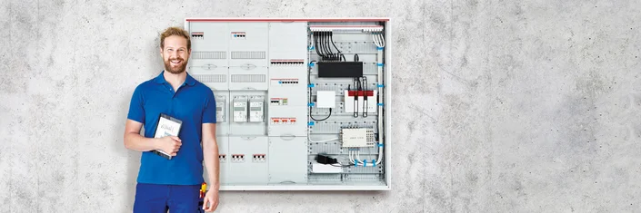 Das Bild zeigt eine Person, die vor einem Schaltschrank steht, der geöffnet ist.