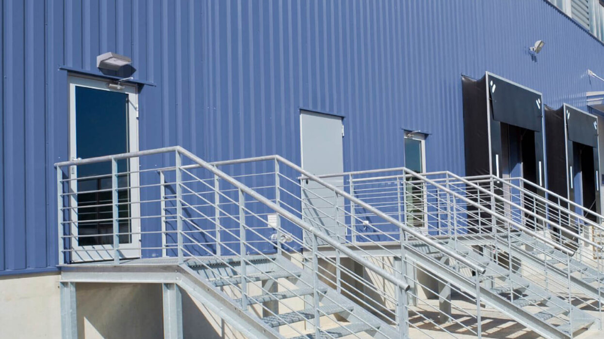 Eaton Outdoor Wall Das Bild zeigt ein Gebäude mit blauer Fassade. Von drei Türen führen jeweils Treppen mit Metallgeländer nach unten