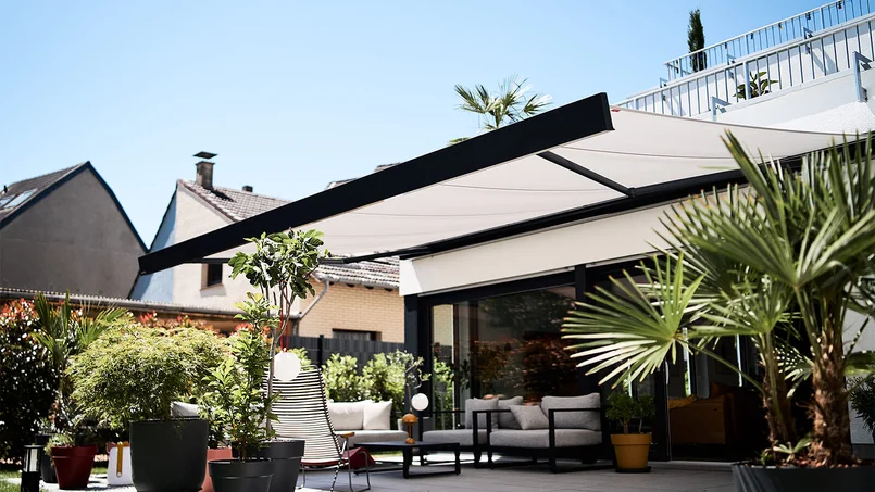 Moderne Terrasse mit ausgefahrener Markise, Sitzmöbeln und bepflanztem Außenbereich an einem Wohnhaus.