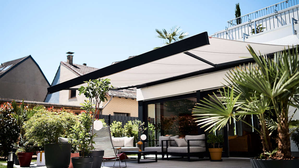Moderne Terrasse mit ausgefahrener Markise, Sitzmöbeln und bepflanztem Außenbereich an einem Wohnhaus.