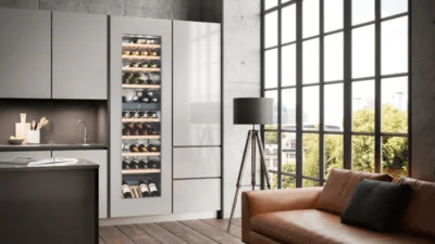 Großer Einbau Weintemperierschrank von Liebherr in der Farbe Cremeweiss und integriert in eine Wohnzimmerschrank-Fläche. Davor ein elegantes Ledersofa in der Farbe hellbraun.