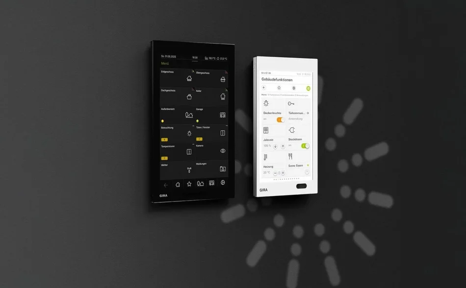 Das Bild zeigt zwei nebeneinander an einer Wand montierte Touch-Bedienpanels, eines in Schwarz und eines in Weiß, beide mit Benutzeroberflächen und dem GIRA-Logo. Auf den Displays sind verschiedene Symbole, Menüs und Steuerungsoptionen zu sehen.
