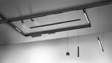 Das Bild zeigt ein an der Decke befestigtes, schwarzes Schienensystem mit Strahlern und Pendelleuchten.