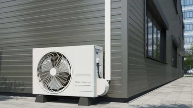 Das Bild zeigt eine außen am Gebäude installierte weiße Wärmepumpen- oder Klimaanlagen-Außeneinheit (Dual Inverter) auf zwei Sockeln. Die Zuleitung verläuft in einem weißen, senkrechten Kabelkanal an der Fassade und führt geschützt in das Gerät.