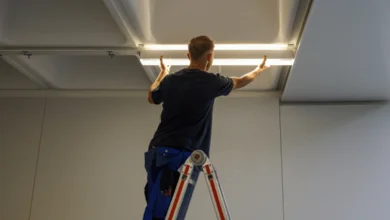 Das Bild zeigt eine Person auf einer Leiter, die eine längliche LED-Leuchte unter einer Raumdecke befestigt. 