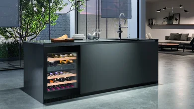 Schwarze elegante Kücheninsel mit ebenfalls schwarzem Weihnkühlschrank, der von innen beleuchtet ist. Im Hintergrund stilvolle Wohnfläche.