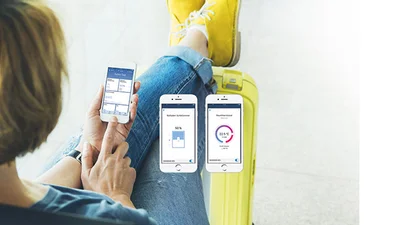 Person von hinten betrachtet, die die Beine nach oben locker überschlagen hat und ein Smartphone in der Hand hält.