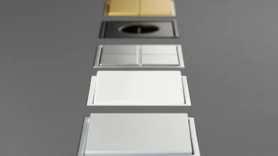 Das Bild zeigt eine Serie von fünf Schalter in verschiedenen Ausführungen, die vertikal auf einem grauen Untergrund angeordnet sind. Die Oberflächen reichen von Gold über Schwarz und Edelstahl bis hin zu Weiß und Silber, was die Vielfalt der Designoptionen hervorhebt.