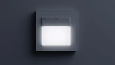 Das Bild zeigt einen dunklen Gira Sensotec LED an einer dunklen Wand.