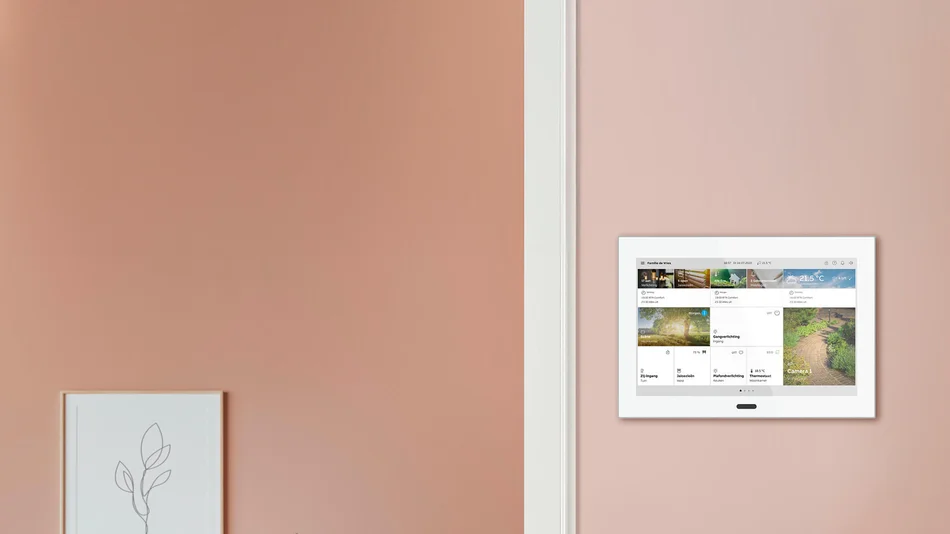 Das Bild zeigt eine moderne, rosa gestrichene Wand mit einem weißen Smart-Home-Bedienpanel, das verschiedene Hausfunktionen anzeigt.