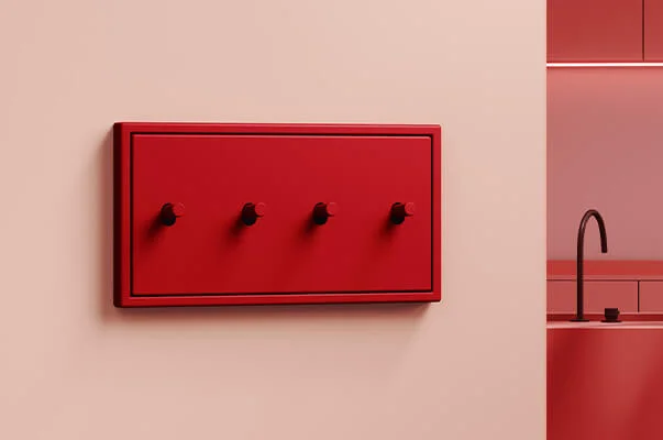 Das Bild zeigt eine moderne, minimalistische Küche in Rottönen. Im Vordergrund befindet sich ein rotes Bedienfeld mit vier Drehknöpfen an der Wand, im Hintergrund eine Küchenzeile mit Spüle und dezentem Licht.