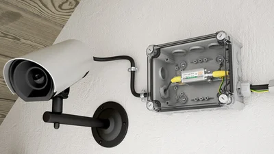 Befestigte Überwachungskamera in der Farbe Weiß an einer ebenfalls weißen Wand.